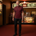 Man in a checkered shirt standing in a movie theater lobby with movie posters on the wall.